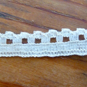 May include: White cotton lace trim with a scalloped edge and small square cutouts.