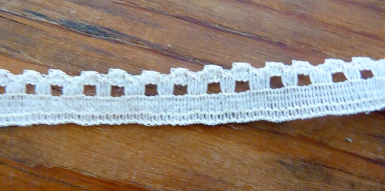 May include: White cotton lace trim with a scalloped edge and small square cutouts.