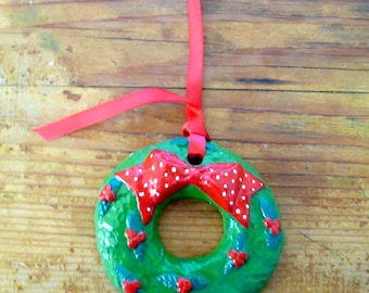May include: A green Christmas wreath ornament with a red bow with white polka dots. The ornament has a red ribbon for hanging.