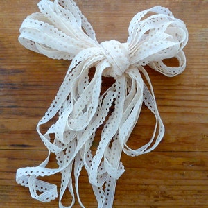 May include: A white crocheted lace trim ribbon tied in a bow. The ribbon is made of a delicate, openwork fabric with a scalloped edge.
