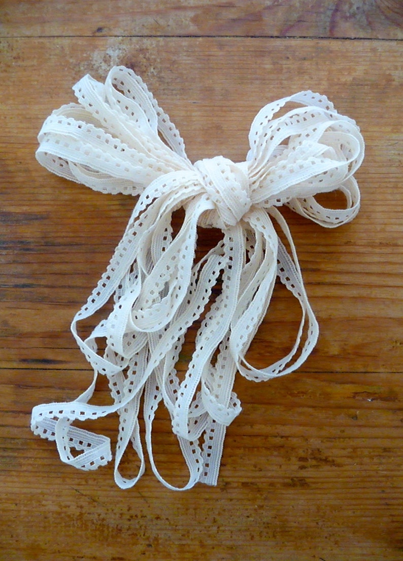 May include: A white crocheted lace trim ribbon tied in a bow. The ribbon is made of a delicate, openwork fabric with a scalloped edge.
