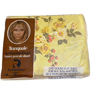 May include: A packaged double flat sheet by Dan River. The sheet is yellow with a floral pattern of yellow and pink flowers. The packaging includes a label with the brand name "Tranquale" and the text "No Iron Dan-Press luxury percale sheet". The sheet is for a 54 x 76 in. mattress.