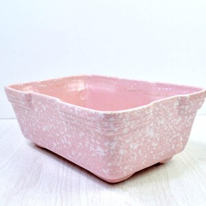 May include: A rectangular pink ceramic planter with a speckled white pattern. The planter has a slightly textured surface and a simple, classic design. It is elevated on small feet and suitable for indoor or outdoor use.