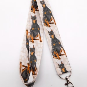 May include: White lanyard with a repeating pattern of black and brown Doberman Pinschers. The lanyard has a silver swivel clip.