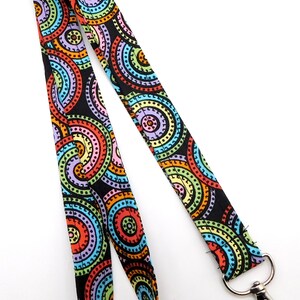 May include: A colorful lanyard with a repeating pattern of concentric circles in shades of red, orange, yellow, green, blue, and purple on a black background. The lanyard has a silver-colored metal clasp and key ring.