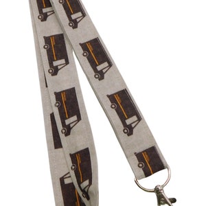 May include: A gray lanyard with a repeating pattern of brown delivery trucks printed on it. The lanyard has a silver metal clip and a silver metal ring.