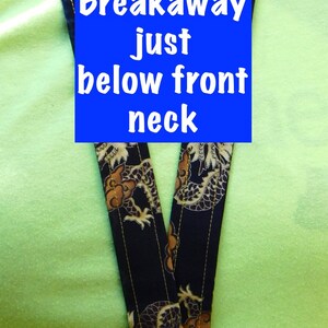 May include: A black and gold lanyard with a dragon pattern. The lanyard has a breakaway clasp just below the front neck.
