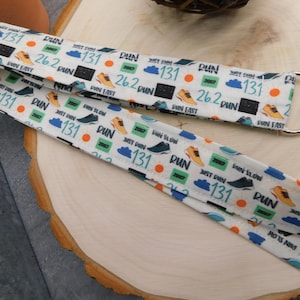 May include: White lanyard with a repeating pattern of running shoes, clouds, and the words "RUN", "131", "26.2", and "2007". The lanyard has a silver-colored metal clasp.