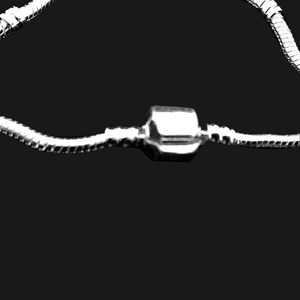 Puede incluir: Una pulsera de cadena de serpiente en tono plateado con un cierre de barril cil&iacute;ndrico y liso en el centro. La cadena flexible tiene una apariencia segmentada y texturizada, curvada en un bucle parcial sobre un fondo negro s&oacute;lido.