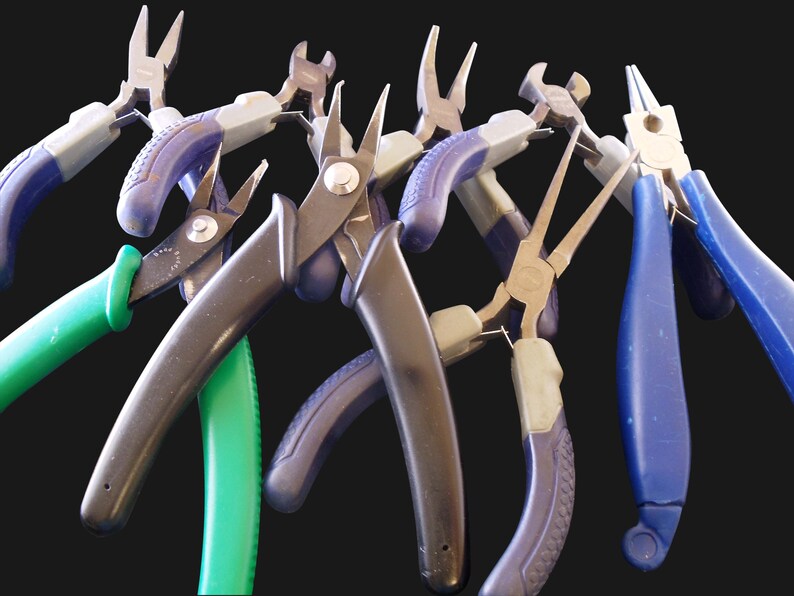 Puede incluir: Una colecci&oacute;n de varios alicates de metal con mangos ergon&oacute;micos en azul, verde y negro. El conjunto incluye alicates de punta fina, cortadores de alambre y alicates de punta plana con agarres texturizados, dispuestos en abanico.
