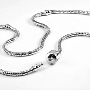 Puede incluir: Un collar de cadena de serpiente en tono plateado con una construcci&oacute;n de metal lisa y flexible y un mecanismo de cierre cil&iacute;ndrico. La cadena incluye dos peque&ntilde;as estaciones met&aacute;licas fijas a lo largo, dise&ntilde;adas para sujetar abalorios.