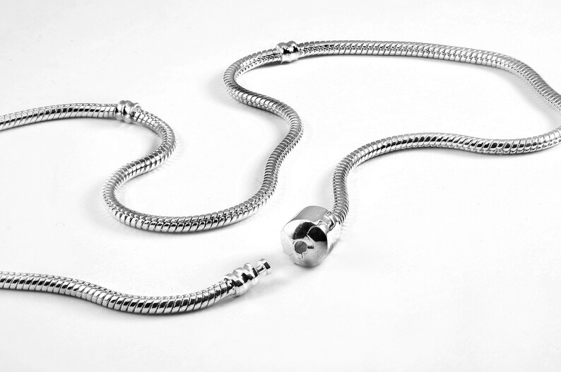 Puede incluir: Un collar de cadena de serpiente en tono plateado con una construcci&oacute;n de metal lisa y flexible y un mecanismo de cierre cil&iacute;ndrico. La cadena incluye dos peque&ntilde;as estaciones met&aacute;licas fijas a lo largo, dise&ntilde;adas para sujetar abalorios.