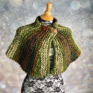May include: A green, brown, and beige knitted cape with wooden buttons. The cape is on a white dress form.