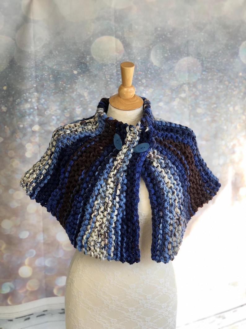 May include: A blue, brown, and white striped knitted shawl with two blue buttons.