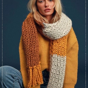 May include: A chunky knit scarf with brown, white, and mustard yellow stripes. The scarf is worn by a person with blonde hair and is styled with a yellow sweater and blue jeans.