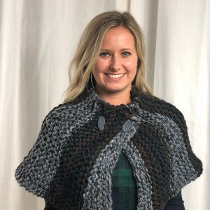 May include: A gray, brown, and black knitted shawl with two buttons. The shawl is worn by a person with long blonde hair.