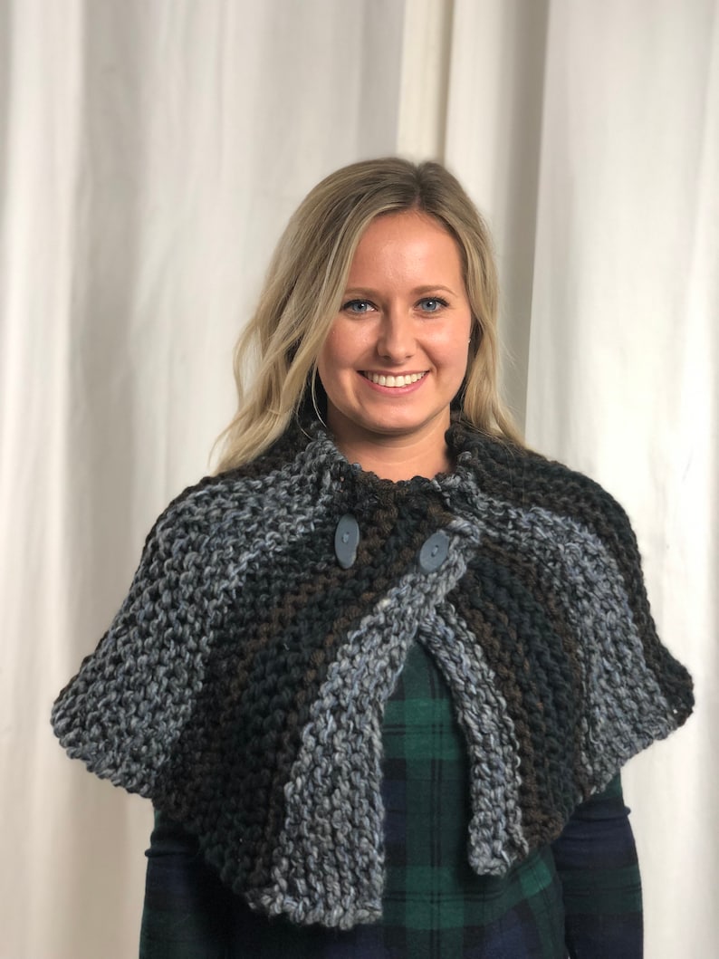 May include: A gray, brown, and black knitted shawl with two buttons. The shawl is worn by a person with long blonde hair.