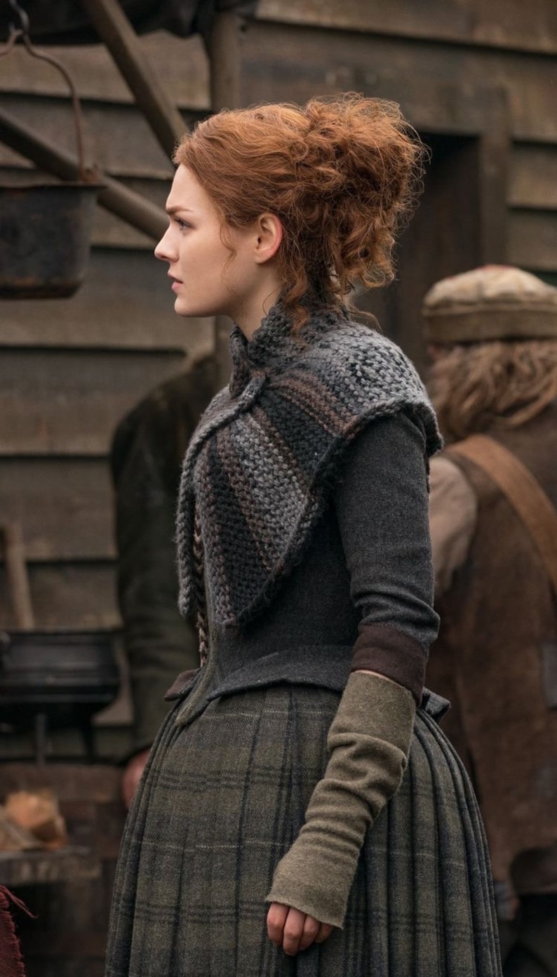 May include: A woman with red curly hair wearing a gray knitted shawl with brown stripes, a gray long-sleeved dress with a plaid pattern, and brown leather gloves.
