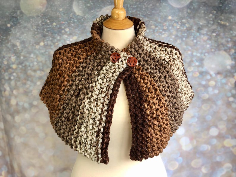 May include: A brown, beige, and cream striped knitted shawl with a high collar and two wooden buttons.