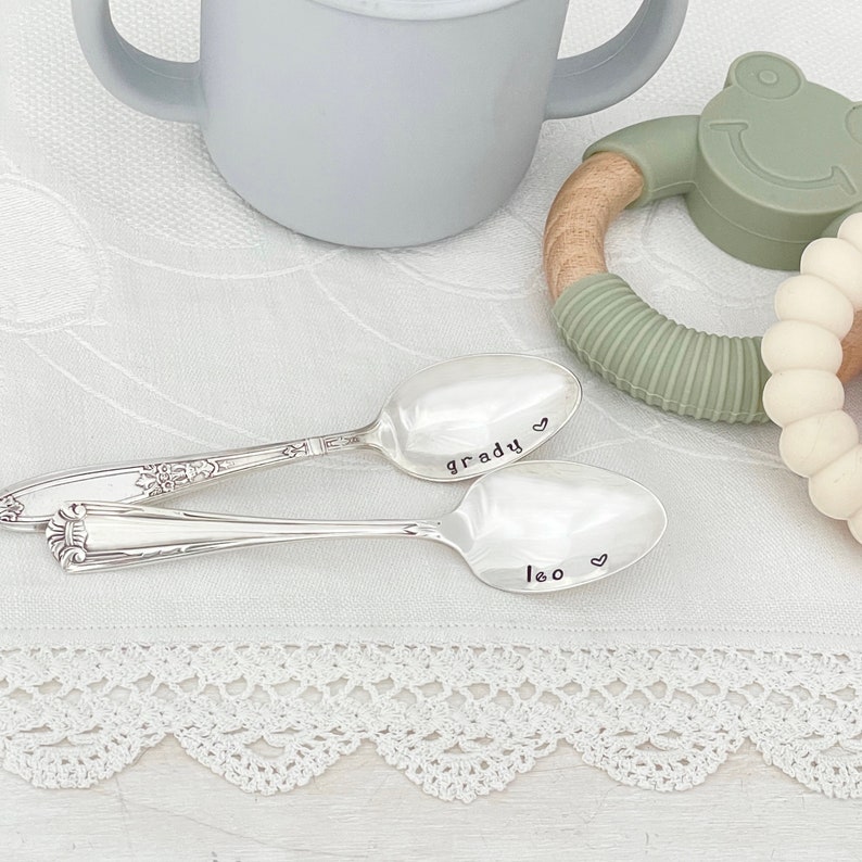 May include: Two silver spoons with personalized engravings. The first spoon says "Grady" with a heart symbol. The second spoon says "Leo" with a heart symbol.