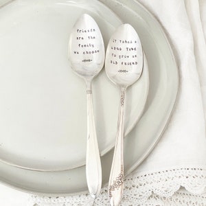 May include: Two silver spoons with engraved sayings. The first spoon says "Friends are the family we choose". The second spoon says "It takes a long time to grow an old friend".