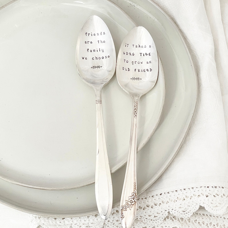 May include: Two silver spoons with engraved sayings. The first spoon says "Friends are the family we choose". The second spoon says "It takes a long time to grow an old friend".