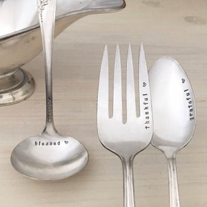 May include: Three silver utensils with engraved words. A ladle with the word "blessed" and a heart, a fork with the word "thankful" and a heart, and a spoon with the word "grateful" and a heart.
