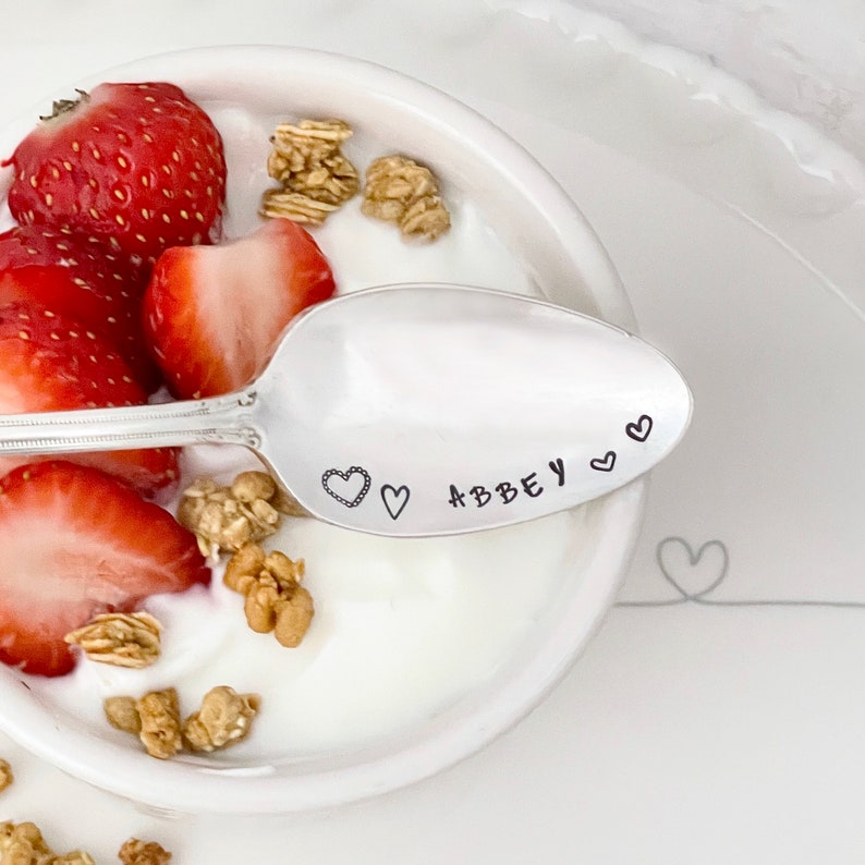 Pu&ograve; includere: Un cucchiaio d'argento con il nome "Abbey" inciso su di esso, circondato da cuori. Il cucchiaio &egrave; in una ciotola di yogurt con fragole e granola.