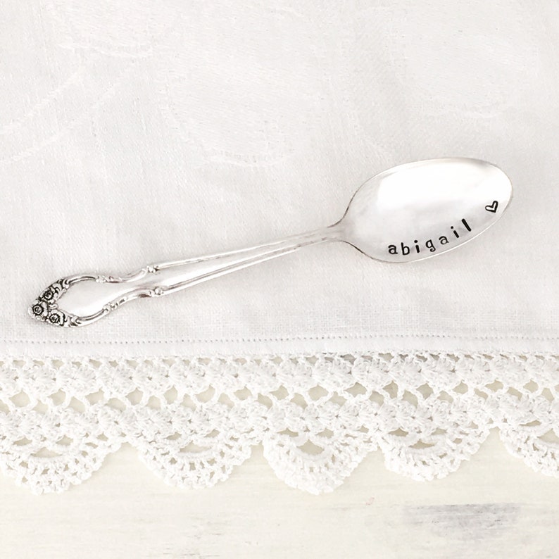 May include: A silver spoon with the name "abigail" engraved on it, with a small heart symbol next to the name.