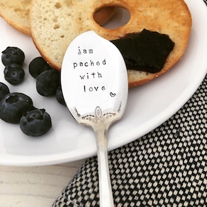 May include: A silver spoon with a decorative handle and the words "jam packed with love" engraved on the bowl. A heart symbol is also engraved on the spoon.
