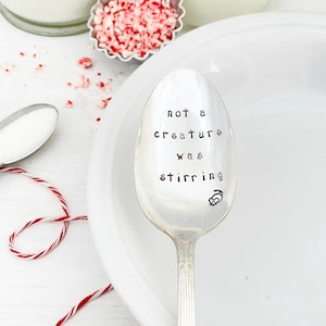 May include: A silver spoon with the phrase "not a creature was stirring" engraved on it. The spoon is sitting on a white plate.