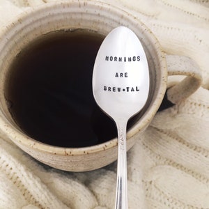 May include: A silver spoon with the words "Mornings are Brew-tal" engraved on it. The spoon is resting in a mug of coffee.