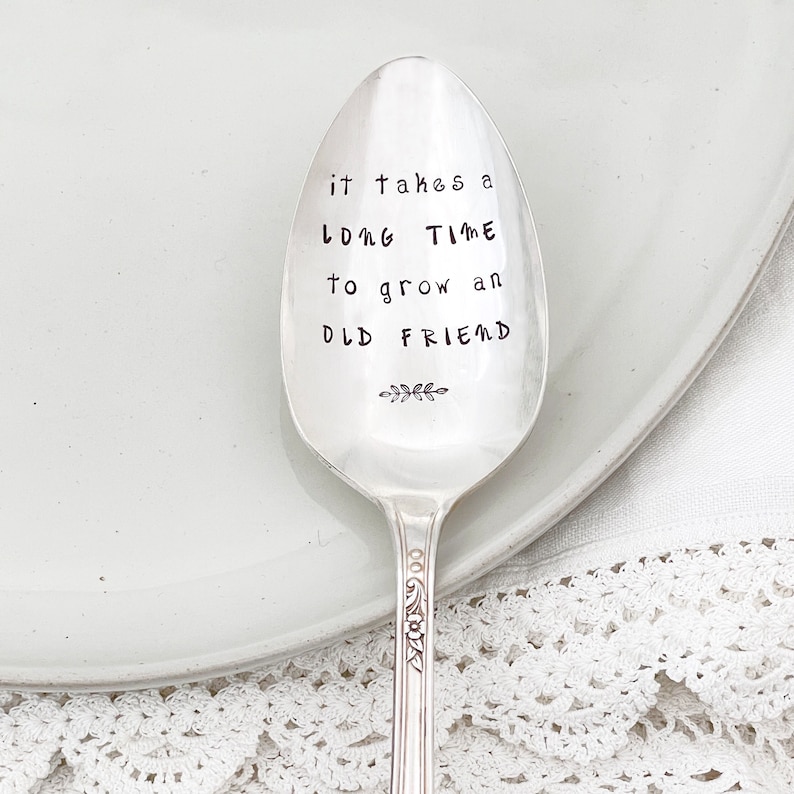 May include: A silver spoon with the inscription "it takes a long time to grow an old friend" and a small sprig of leaves.
