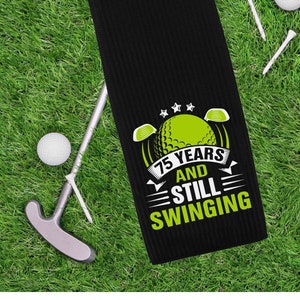 May include: Black golf towel with a green and white graphic that says "75 Years and Still Swinging".