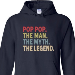 May include: Navy blue hooded sweatshirt with the text "POP POP. THE MAN. THE MYTH. THE LEGEND." in red, blue, and tan lettering. The sweatshirt has a front pocket and a drawstring hood.