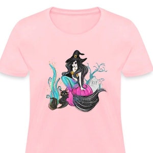 Puede incluir: Una camiseta rosa para mujer con un gráfico de una bruja con un gato negro sentado en una calabaza. La bruja lleva un sombrero negro y tiene el pelo largo y negro. El fondo es un cementerio con una lápida que dice "RIP".
