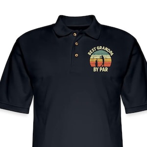 May include: Black polo shirt with a vintage-style graphic that says "Best Grandpa By Par" with a silhouette of a golfer and a sunset.