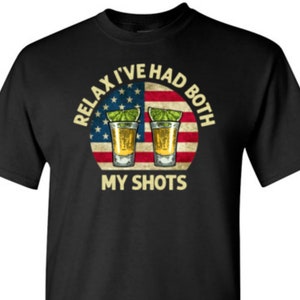May include: Black t-shirt with a white, red, and blue American flag design. The text "Relax I've Had Both My Shots" is written in a yellow font around the flag.