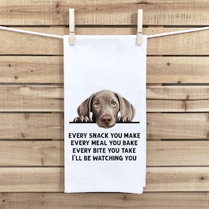 May include: A white kitchen towel with a brown and gray Weimaraner dog peeking over the top. The text on the towel reads "Every snack you make, every meal you bake, every bite you take, I'll be watching you."