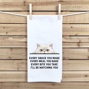 May include: White kitchen towel with a white cat peeking over the top. The text on the towel reads "Every snack you make, every meal you bake, every bite you take, I'll be watching you."