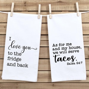 May include: Two white kitchen towels with black text. The first towel says "I love you to the fridge and back". The second towel says "As for me and my house, we will serve tacos. Salsa 24:7".