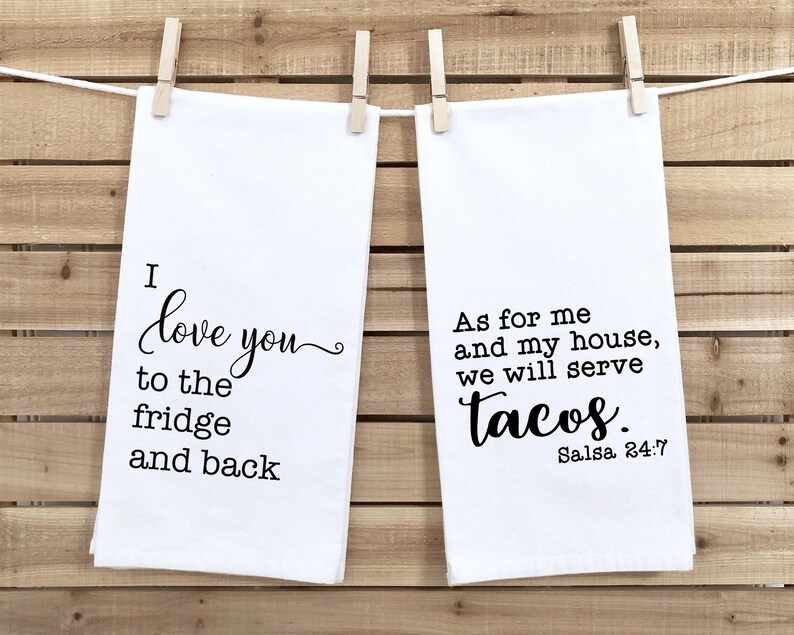May include: Two white kitchen towels with black text. The first towel says "I love you to the fridge and back". The second towel says "As for me and my house, we will serve tacos. Salsa 24:7".