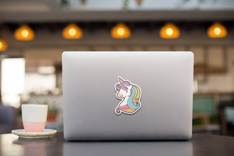May include: A white unicorn with a rainbow mane and tail is depicted on a laptop sticker. The unicorn has a pink nose and a brown horn.