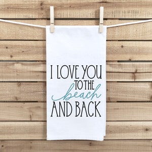 May include: White kitchen towel with black text that reads "I love you to the beach and back". The word "beach" is written in teal.