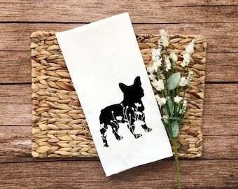 May include: A white kitchen towel with a black silhouette of a French bulldog with white flowers inside the silhouette.