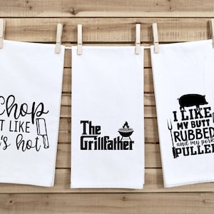 May include: Three white kitchen towels with black text and graphics. The first towel says "Chop it like it's hot" with a black knife graphic. The second towel says "The Grillfather" with a black grill graphic. The third towel says "I like my butt rubbed and my pork pulled" with a black pig graphic and a black grill tool graphic.