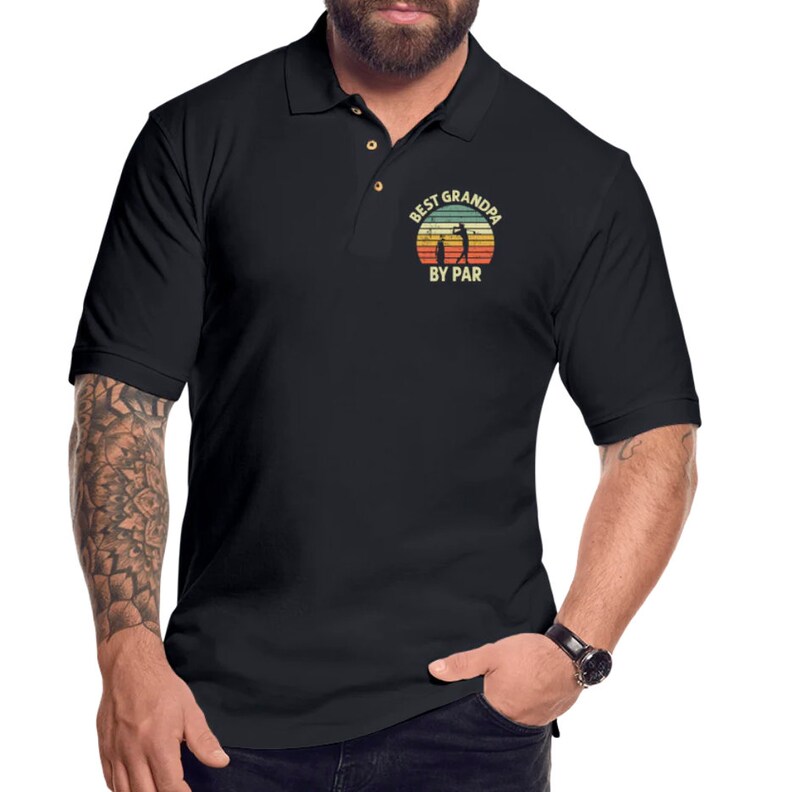 May include: Black polo shirt with a vintage-style graphic that says "Best Grandpa By Par" with a silhouette of a golfer and a child golfer.