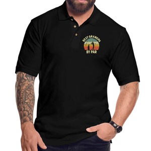 May include: Black polo shirt with a vintage-style graphic that says "Best Grandpa By Par" with a silhouette of a golfer.