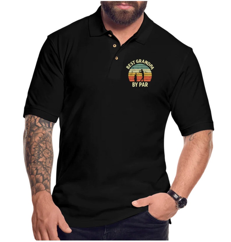 May include: Black polo shirt with a vintage-style graphic that says "Best Grandpa By Par" with a silhouette of a golfer.