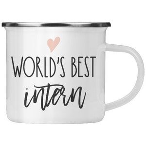 May include: White enamel mug with a silver rim and a pink heart. The mug says "World's Best Intern" in black lettering.